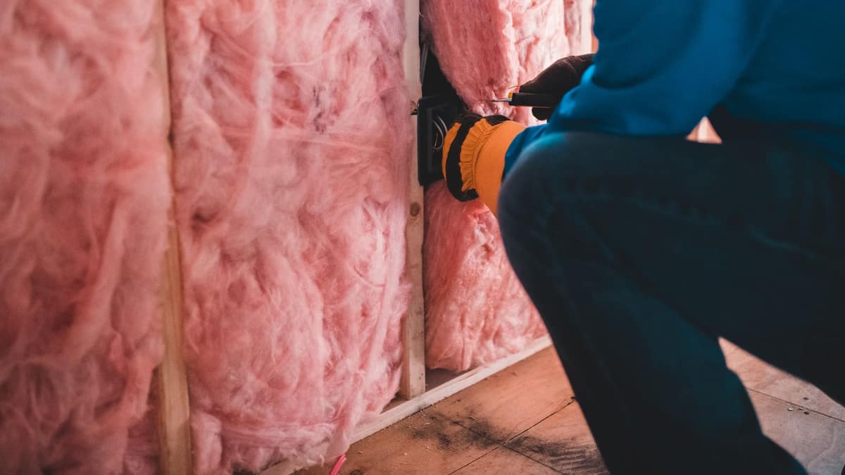 Installer working in an attic between insulation and roof framing, where attic ventilation is planned